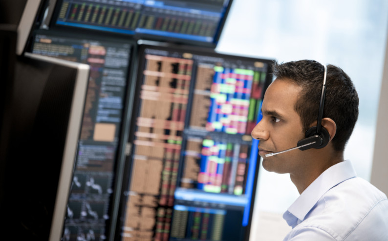 A man wearing a headset is sitting in front of multiple monitors